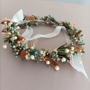 delicate floral crown made with dried flowers in shades of brown, white, and blue. The crown is tied with a white ribbon and features small, dried flowers and leaves.