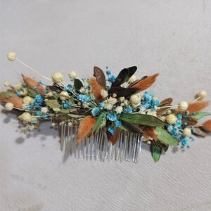 May include: A floral hair comb featuring a variety of dried flowers in shades of brown, orange, blue, and green. The comb has a clear plastic base with multiple teeth, and the flowers are arranged in a decorative pattern.