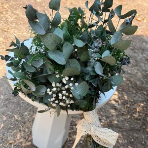 Pode incluir: Um buqu&ecirc; de folhas de eucalipto secas e pequenas flores brancas de gips&oacute;fila, amarrado com uma fita de renda na cor creme. Os caules est&atilde;o reunidos na base e a folhagem apresenta tons verdes e cinzentos suaves em todo o arranjo.