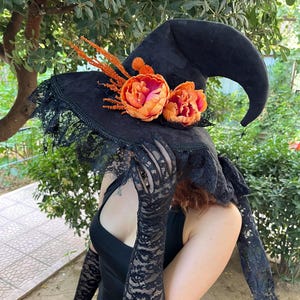 May include: A black witch hat with a wide brim, adorned with orange and pink flowers and lace trim. The hat has a pointed crown and is decorated with orange sprigs. The hat is a costume accessory.