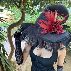 May include: A black witch hat with a wide brim, adorned with red leaves and a flower. The hat has a lace trim and is paired with black lace gloves. The overall theme is gothic and Halloween.