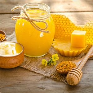 May include: A wooden table with a jar of honey, a bowl of honey, a honeycomb, a small dish of pollen, and two wooden honey dippers. The honey is a light golden color and the honeycomb is a dark golden color.