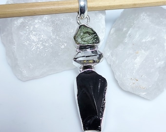 May include: A silver pendant featuring a black obsidian stone, a clear quartz crystal, and a green aventurine stone. The pendant is designed in a stacked, layered style.