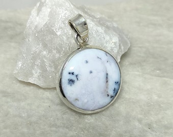 May include: A silver pendant with a white and black dendritic agate stone. The stone is round and has a smooth surface. The pendant is on a white background.