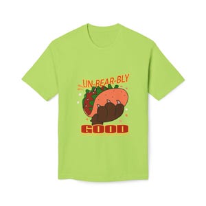 May include: Lime green t-shirt featuring a cartoon taco held by a bear paw. The text "UN-BEAR-BLY GOOD" is above and below the graphic. The taco has lettuce, tomato, and a bun. The bear paw is brown.