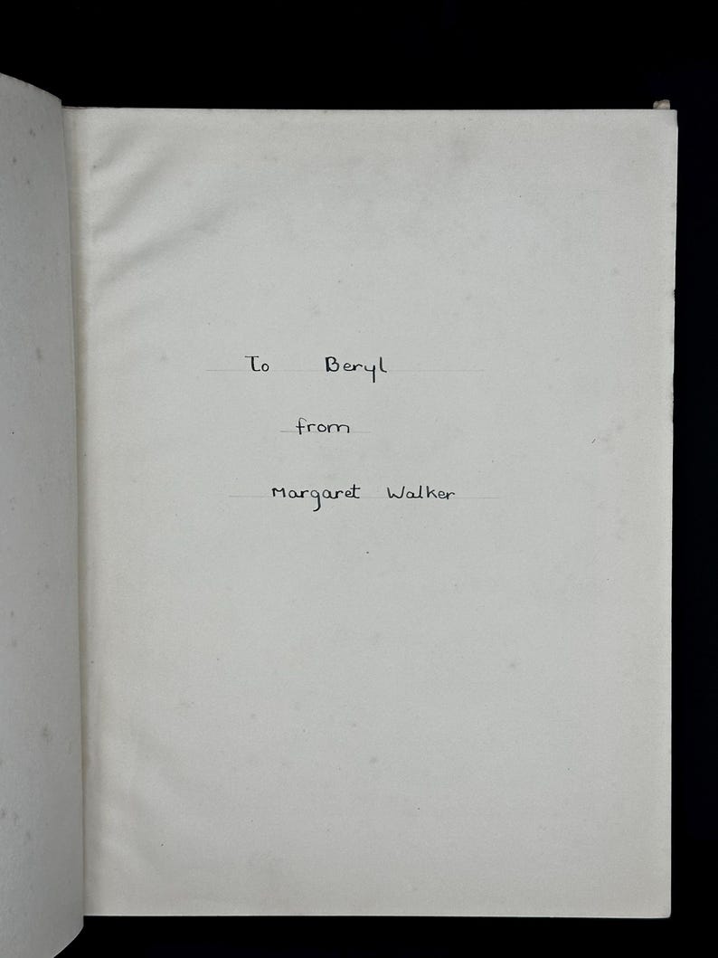 May include: An open book page with handwritten text. The text reads "To Beryl from Margaret Walker" in black ink. The paper is off-white and slightly textured, with a visible crease.