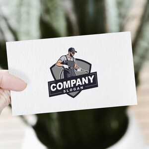Pode incluir: Um design de logotipo com uma ilustra&ccedil;&atilde;o de desenho animado de uma pessoa usando um bon&eacute; e segurando uma lavadora de alta press&atilde;o. O logotipo est&aacute; sobre um escudo cinza com o texto "COMPANY" e "SLOGAN" abaixo.