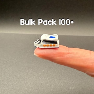May include: A miniature white cruise ship figurine featuring black horizontal stripes, orange accents along the side, and a blue top detail. The text Bulk Pack 100+ is displayed above the object, which is shown resting on a fingertip.