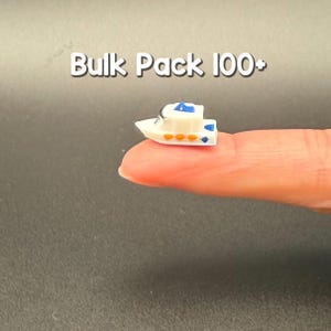 May include: A miniature white boat figurine with blue and orange accents, featuring the text Bulk Pack 100+ above it. The small vessel has a cabin structure, a pointed bow, and a flat stern, presented as a bulk pack item for various craft projects.