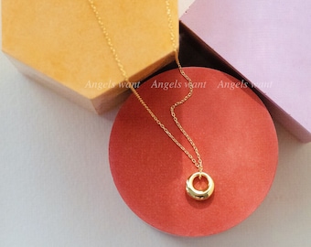 May include: A gold chain necklace with a thick, round, gold pendant. The necklace is displayed on a red circular surface.