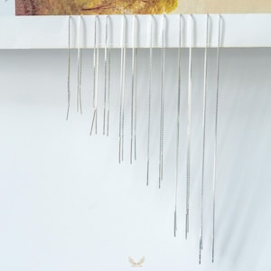 May include: A collection of silver threader earrings displayed against a white background. The earrings are long, delicate chains with a small bar at the end. The earrings are arranged in a descending order, creating a visual cascade.