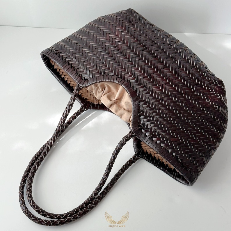 May include: A dark brown woven tote bag with braided handles. The bag has a rectangular shape with a woven pattern and a light brown interior lining. The handles are also dark brown and braided.