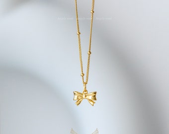 May include: A gold chain necklace with a small gold bow pendant. The chain has a delicate, beaded design.