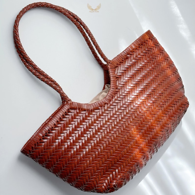May include: A brown woven tote bag with braided handles. The bag has a rectangular shape with a wide opening and a light-colored interior. The woven pattern creates a textured surface.