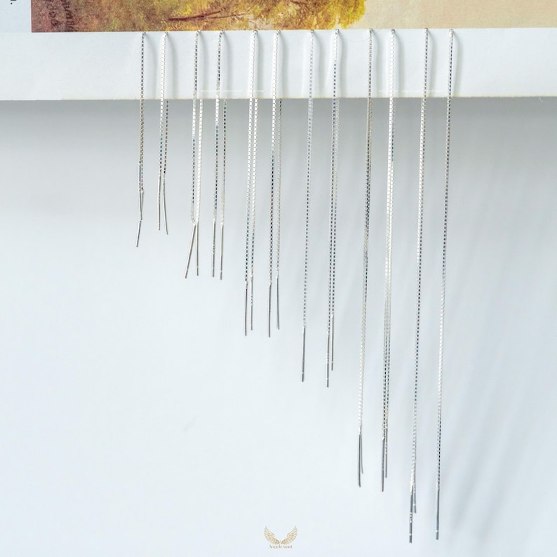 Puede incluir: Una colecci&oacute;n de pendientes de hilo plateados exhibidos sobre un fondo blanco. Los pendientes son cadenas largas y delicadas con una peque&ntilde;a barra en el extremo. Los pendientes est&aacute;n dispuestos en orden descendente.