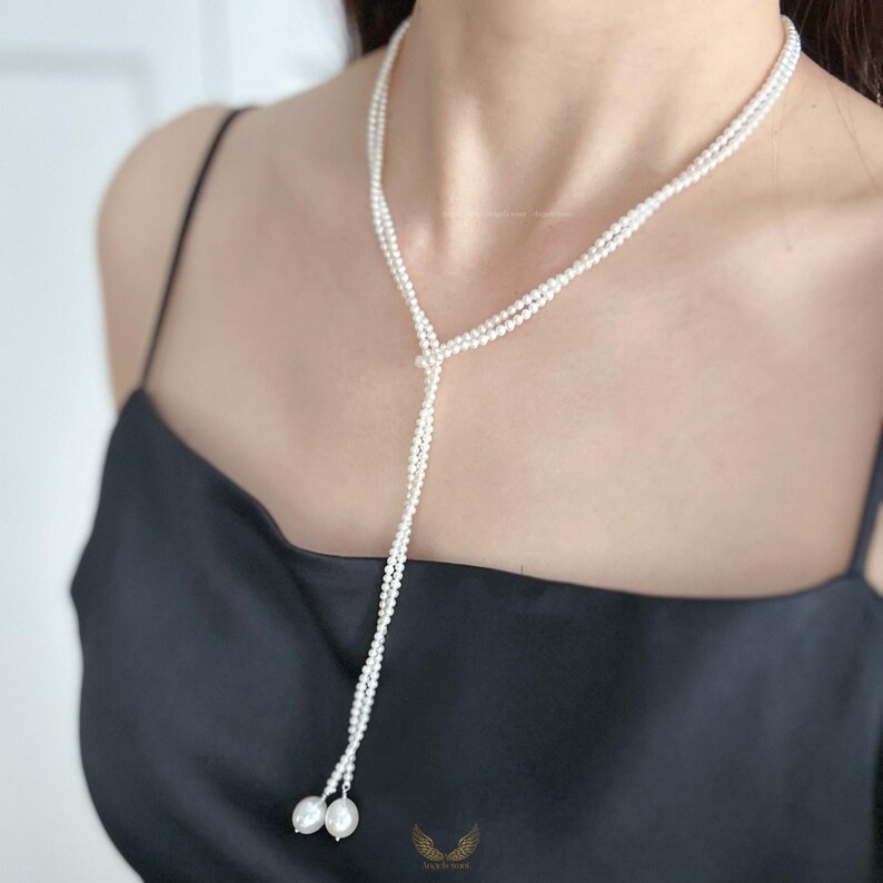 May include: A delicate pearl necklace with a Y-shaped design. The necklace features multiple strands of small, white pearls that converge at the center and cascade down. Two larger pearls dangle at the end of the necklace, adding a touch of elegance. The necklace is worn against a black top.