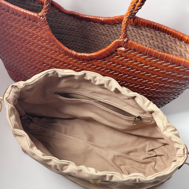May include: A woven brown leather tote bag with braided handles. The bag has a spacious interior and a tan drawstring pouch with a zippered pocket. The bag is designed for carrying items.