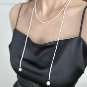 May include: A delicate, layered pearl necklace with a long, draping design. The necklace features small, round pearls and larger, teardrop-shaped pearls at the ends. The jewelry is displayed against a black background.