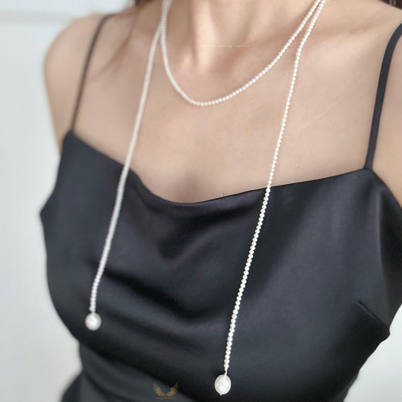 May include: A delicate, layered pearl necklace with a long, draping design. The necklace features small, round pearls and larger, teardrop-shaped pearls at the ends. The jewelry is displayed against a black background.