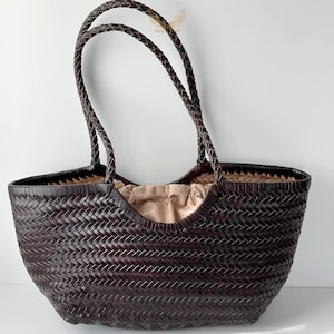 May include: A dark brown woven tote bag with braided handles. The bag has a spacious interior with a light tan fabric lining. The woven pattern creates a textured surface, and the handles are securely attached. This stylish bag is suitable for everyday use.