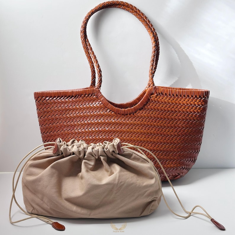 May include: A woven brown leather tote bag with braided handles and a matching drawstring pouch. The tote bag has a rectangular shape with a wide opening. The drawstring pouch is beige and has a leather pull.