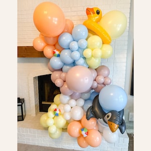 May include: A balloon arch made of pastel colored balloons, including peach, light blue, white, and yellow. The arch is decorated with inflatable toys, including a yellow duck and a penguin.