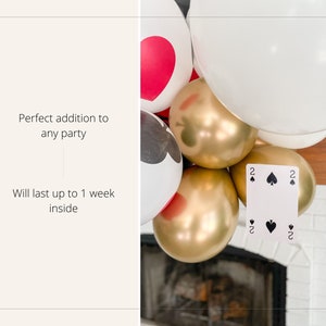 May include: A garland of balloons with a playing card attached. The balloons are white, gold, and red with black card suit symbols. The card is a two of spades.