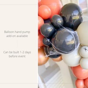 May include: A Halloween-themed balloon garland featuring black, white, and orange balloons. The garland is decorated with faux spiderwebs and small plastic spiders. Text on the left says "Balloon hand pump add-on available" and "Can be built 1-2 days before event."