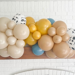 May include: A balloon garland featuring a mix of colors, including beige, yellow, blue, and brown. Some balloons have a dalmatian print. The balloons are arranged in a cluster, suitable for a party or event decoration.