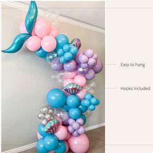 K&ouml;nnte beinhalten: Eine Meerjungfrauen-Ballon-Girlande mit rosa, blauen, violetten und silbernen Ballons. Die Girlande ist mit Muscheln und einem Meerjungfrauen-Schwanz verziert. Einfach aufzuh&auml;ngen mit im Lieferumfang enthaltenen Haken.