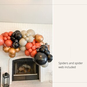 May include: A Halloween-themed balloon garland in shades of orange, black, gold, and beige, arranged above a fireplace. The garland includes spiders and spider webs for decoration.
