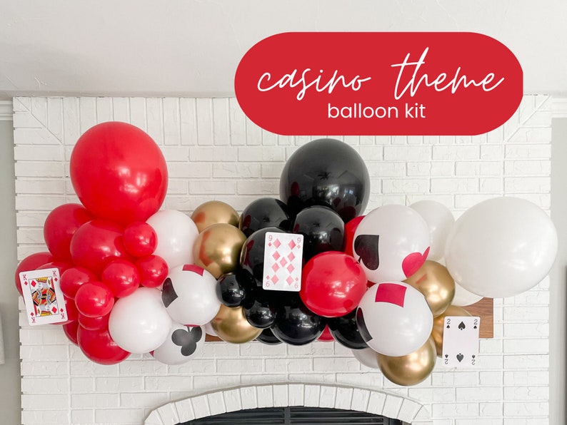 May include: A casino themed balloon arch kit with red, black, white, and gold balloons. The balloons are arranged in a cascading arch shape and include playing card cutouts with hearts, spades, diamonds, and clubs.
