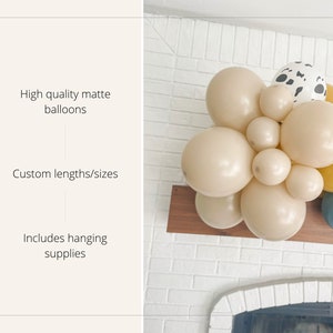 May include: A balloon garland featuring high-quality matte balloons in various sizes and colors, including beige, yellow, and blue. One balloon has a dalmatian print. The garland includes hanging supplies.
