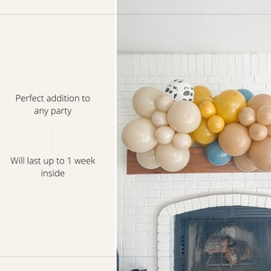 May include: A balloon garland in shades of beige, yellow, and blue, with some balloons featuring a black and white cow print. The garland is arranged on a wooden shelf above a white brick fireplace. Text on the left reads: "Perfect addition to any party".