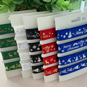 May include: A selection of Christmas ribbons in green, white, black, red, and blue. Each ribbon displays festive designs and the words "Merry Christmas." The ribbons are presented on white card.