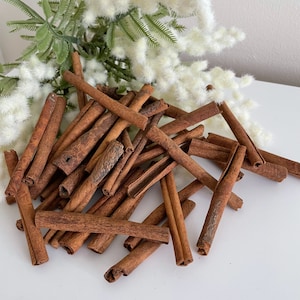 May include: A pile of brown cinnamon sticks on a white surface. The sticks are of various lengths and thicknesses.