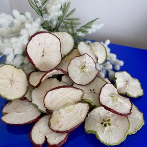 May include: A pile of dried apple slices on a blue surface. The apple slices are a mix of red and green, and some have a red rim.