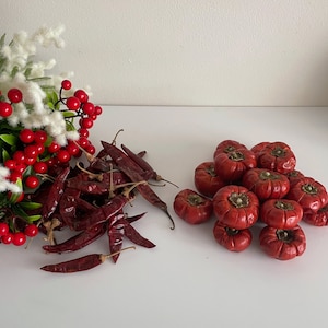 May include: A pile of dried red chilli peppers and a group of red tomatoes. The chilli peppers are arranged in a pile, while the tomatoes are scattered around.
