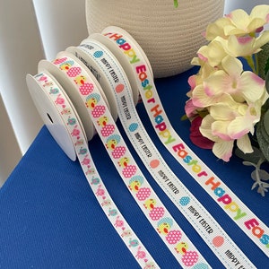 May include: Four rolls of white ribbon with a repeating pattern of colourful chicks and eggs. The ribbon has the text "Happy Easter" printed on it.