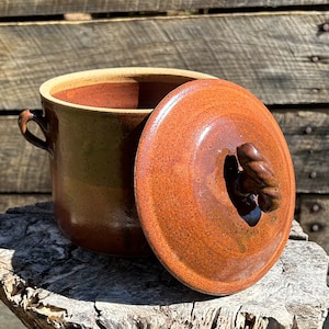 May include: A brown ceramic pot with a lid and two handles. The pot has a speckled glaze and the lid has a twisted knob.