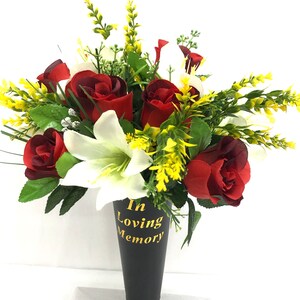 May include: A black cone vase with the words "In Loving Memory" in gold lettering, filled with a bouquet of red roses, white lilies, and yellow greenery.