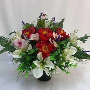 May include: An artificial flower arrangement in a black pot, featuring red, white and green peonies, lilies and other flowers.