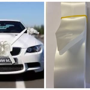 May include: A white car adorned with white bows and ribbons, possibly for a wedding. The car has a number plate reading "BMW M". Next to it, two rolls of white satin ribbon are secured with yellow elastic bands.