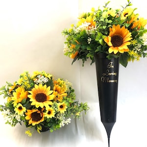 May include: Two floral arrangements with vibrant yellow sunflowers, brown centres, and green foliage. One is in a black vase with "In Loving Memory" in gold script. The other is in a round black container, both arrangements are on a white background.