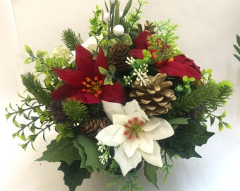 May include: A festive Christmas floral arrangement featuring red and white poinsettias, green foliage, and gold-painted pinecones. The arrangement includes sprigs of greenery and small white berries, creating a holiday centerpiece.