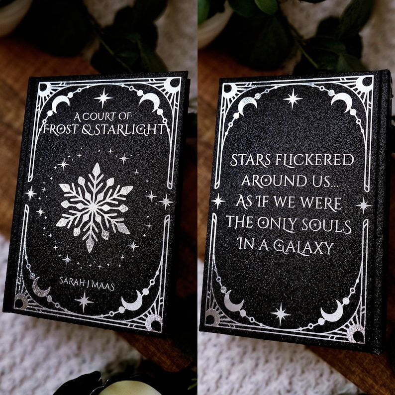 May include: A black book with silver lettering and accents. The cover reads "A Court of Frost & Starlight" with a snowflake design. The spine reads "Stars flickered around us... as if we were the only souls in a galaxy."