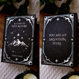 May include: A black book with silver lettering and accents. The front cover reads "A Court of Mist & Fury" above a mountain illustration. The back cover says "You are my salvation Feyre." The author's name, Sarah J. Maas, is on the front.
