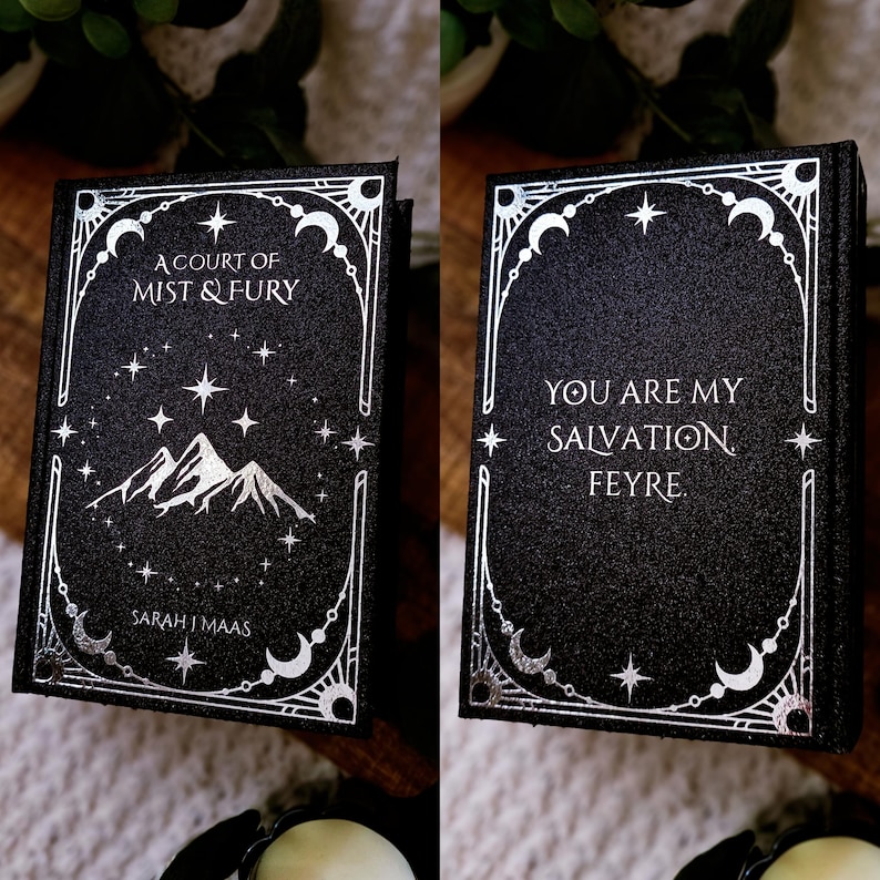 May include: A black book with silver lettering and accents. The front cover reads "A Court of Mist & Fury" above a mountain illustration. The back cover says "You are my salvation Feyre." The author's name, Sarah J. Maas, is on the front.