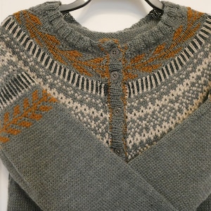 May include: A gray knitted cardigan with a brown and white geometric pattern. The cardigan has a button closure and long sleeves.