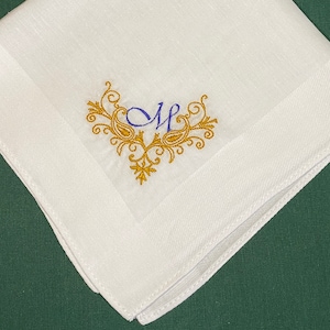 May include: White linen handkerchief with a gold embroidered monogram "M" in a decorative floral design.